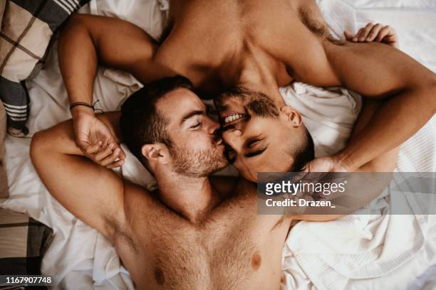 pareja desnuda multi étnica gay en casa besándose en la cama - vista de ángulo alto - hombre gay fotografías e imágenes de stock
