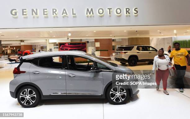 People walk past GM vehicles on display at the General Motors world headquarters building at Detroit's Renaissance Center.