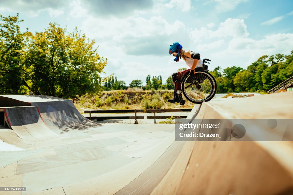 Behinderte Millennial Frau im Rollstuhl rollt die Hügel in Skatepark