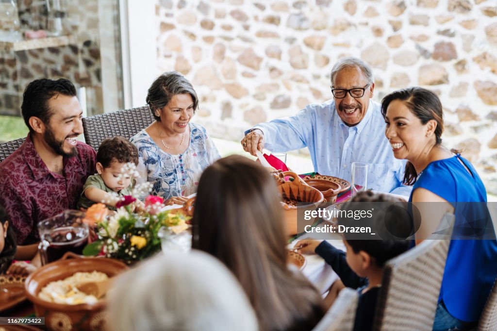 Latin senior man serving the food to his family at dinner table