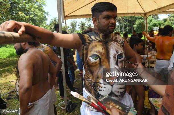 Performer poses for a picture as his body is being painted to adorn the head of a tiger ahead of the 'Pulikali' in Thrissur on September 14, 2019.