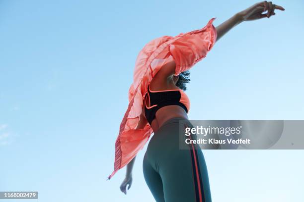 fashionable woman wearing jacket with sports clothing against clear sky - blue coat stock-fotos und bilder