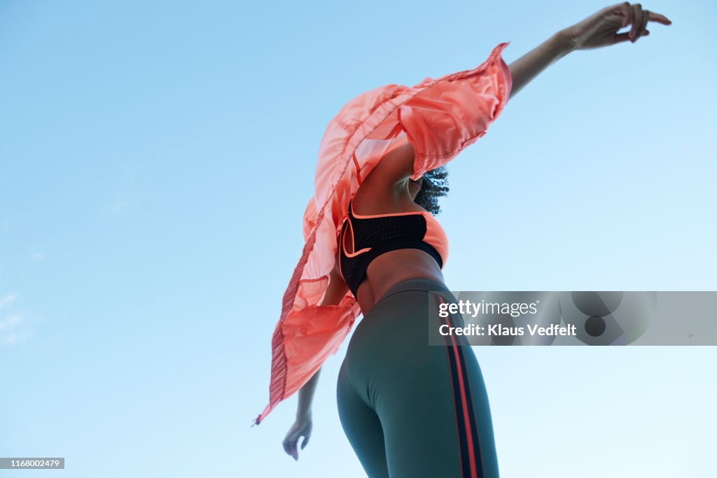 Fashionable woman wearing jacket with sports clothing against clear sky