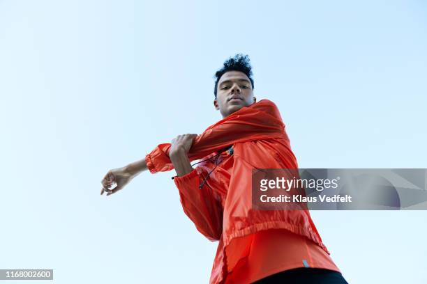 directly below portrait of athlete stretching arm against clear sky - position physique photos et images de collection