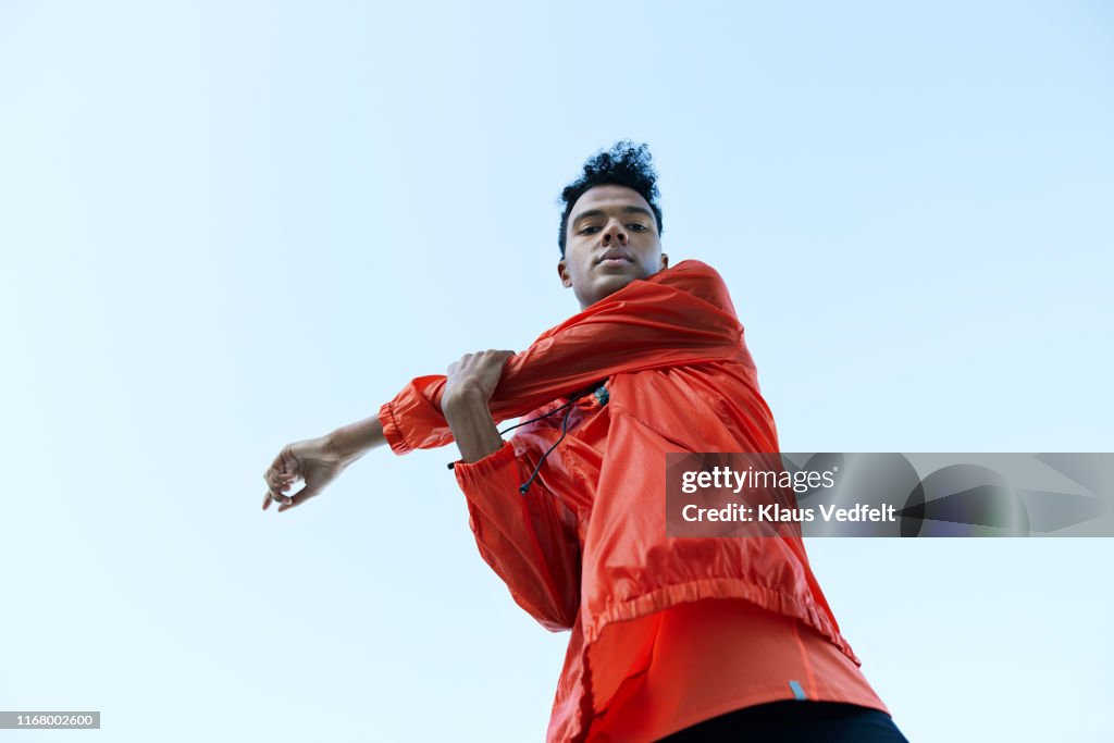 Directly below portrait of athlete stretching arm against clear sky