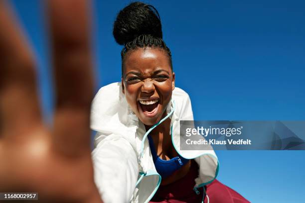 portrait of cheerful young sportswoman with hair bun against clear blue sky - joy stock pictures, royalty-free photos & images