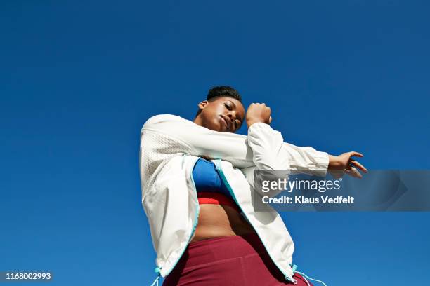 young woman stretching arm against clear blue sky on sunny day - young woman standing against clear sky ストックフォトと画像