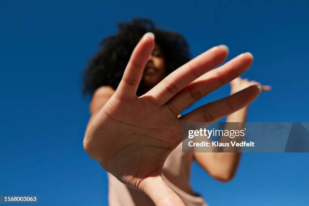 sportswoman showing stop gesture against clear blue sky - hand stop stock-fotos und bilder