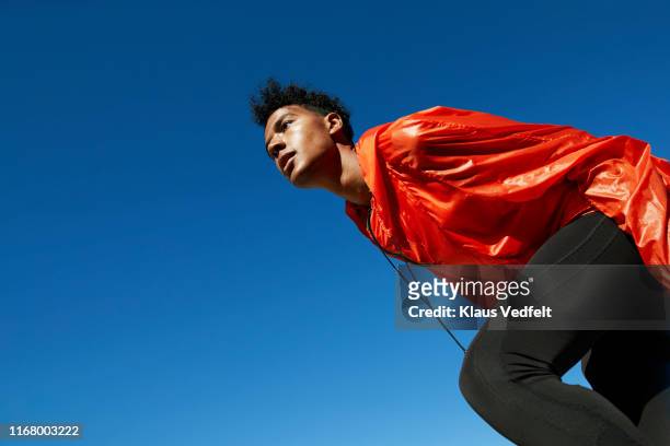 young sportsman looking away against clear blue sky - orange couleur photos et images de collection