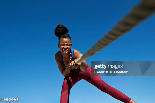 female athlete pulling rope while exercising against clear blue sky - tough lady foto e immagini stock