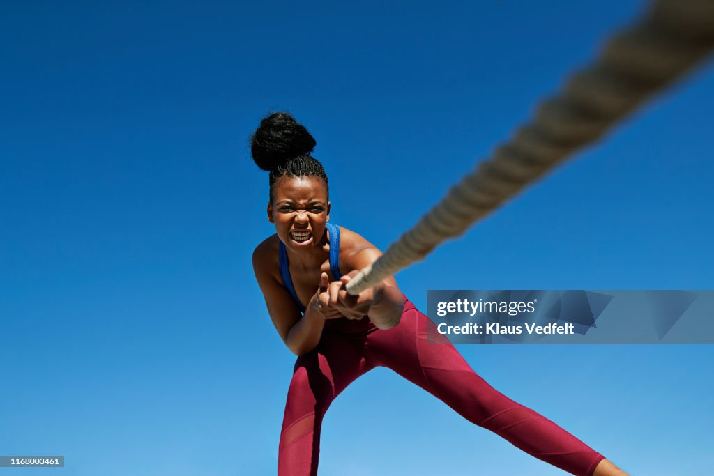 Female athlete pulling rope while exercising against clear blue sky