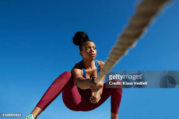 sportswoman pulling rope against clear blue sky on sunny day - cross fit stock-fotos und bilder