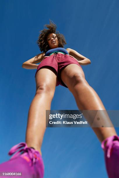 portrait of female athlete wearing shorts with hands on hip against blue sky - running shorts foto e immagini stock