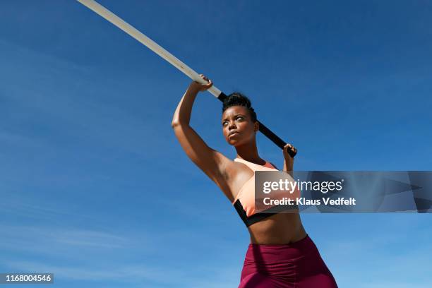 female athlete holding pole vault against blue sky - athlétisme photos et images de collection