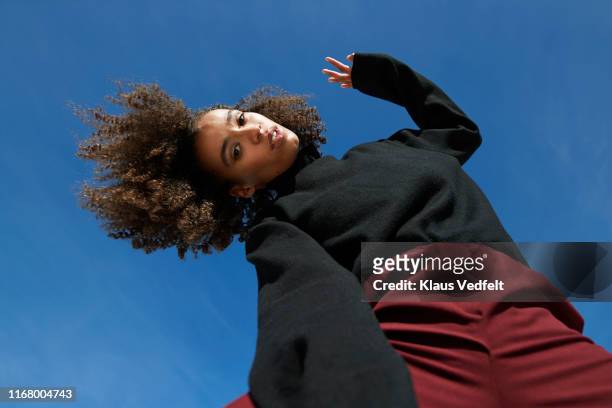 portrait of young woman with head cocked against blue sky - kinky stock-fotos und bilder