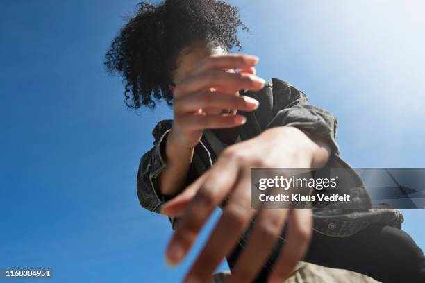 woman wearing denim jacket on rock against blue sky - 曲げる ストックフォトと画像