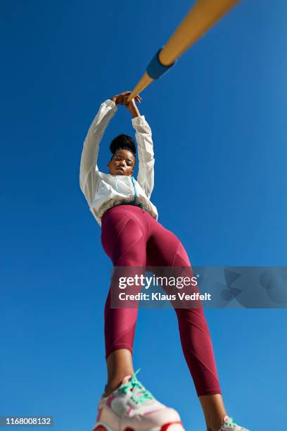 portrait of female athlete holding javelin against clear blue sky - running shoes sky stock-fotos und bilder