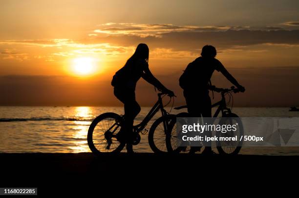 side view of couple standing on seashore with their bicycles and - ipek morel stock pictures, royalty-free photos & images
