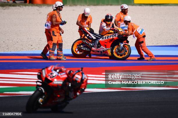 Race marshalls help Repsol Honda Team Spanish rider, Marc Marquez pick his motorbike after he fell, as Ducati Team Italian rider, Danilo Petrucci...