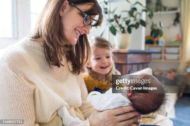 mother holds her newborn baby with older sister watching. - parents baby sister stock pictures, royalty-free photos & images