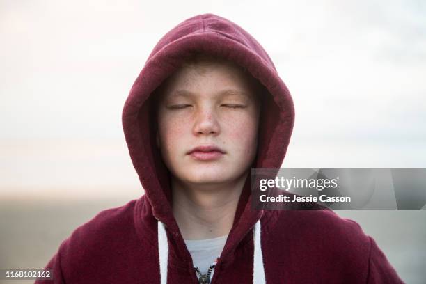 boy with hoodie on beautiful beach with eyes closed in evening light - depressie landelement stockfoto's en -beelden