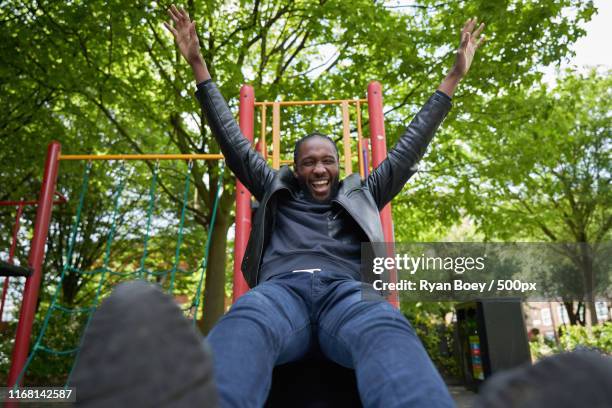 happy man sliding down the slide at a playground - rutsche stock-fotos und bilder