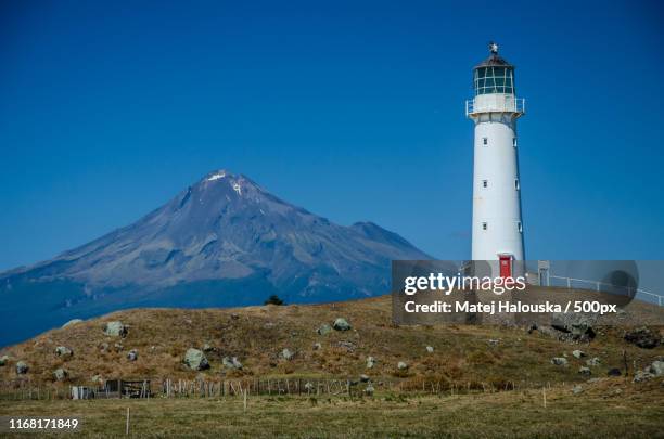 cape egmont lighthouse with mountain taranaki in the background and blue sky above egmont - cape egmont lighthouse stock pictures, royalty-free photos & images