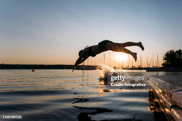 sommertag: junge frau springt bei sonnenuntergang vom steg in den see - taking the plunge stock-fotos und bilder