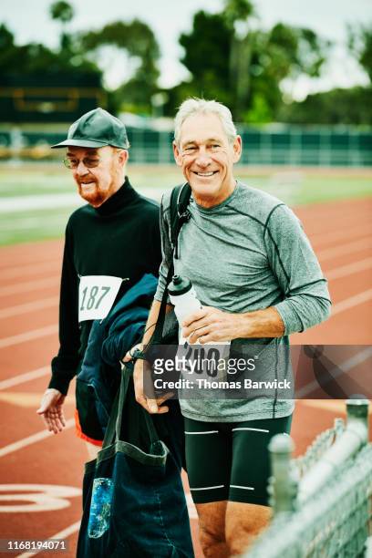 Smiling senior male track athlete walking onto track with friend before meet