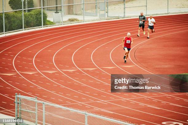 senior male track athletes running distance race on track - forward athlete stock pictures, royalty-free photos & images