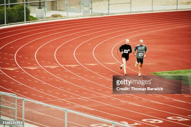 senior male track athletes running distance race on track - coordinated effort stock pictures, royalty-free photos & images