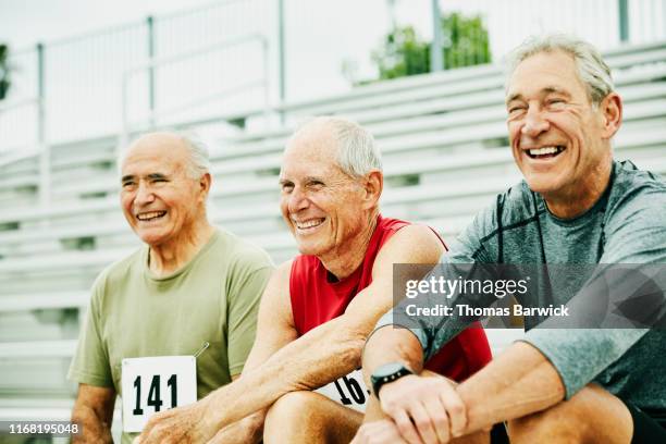 smiling and laughing senior male track athletes hanging out together on bleachers - seulement des hommes seniors photos et images de collection