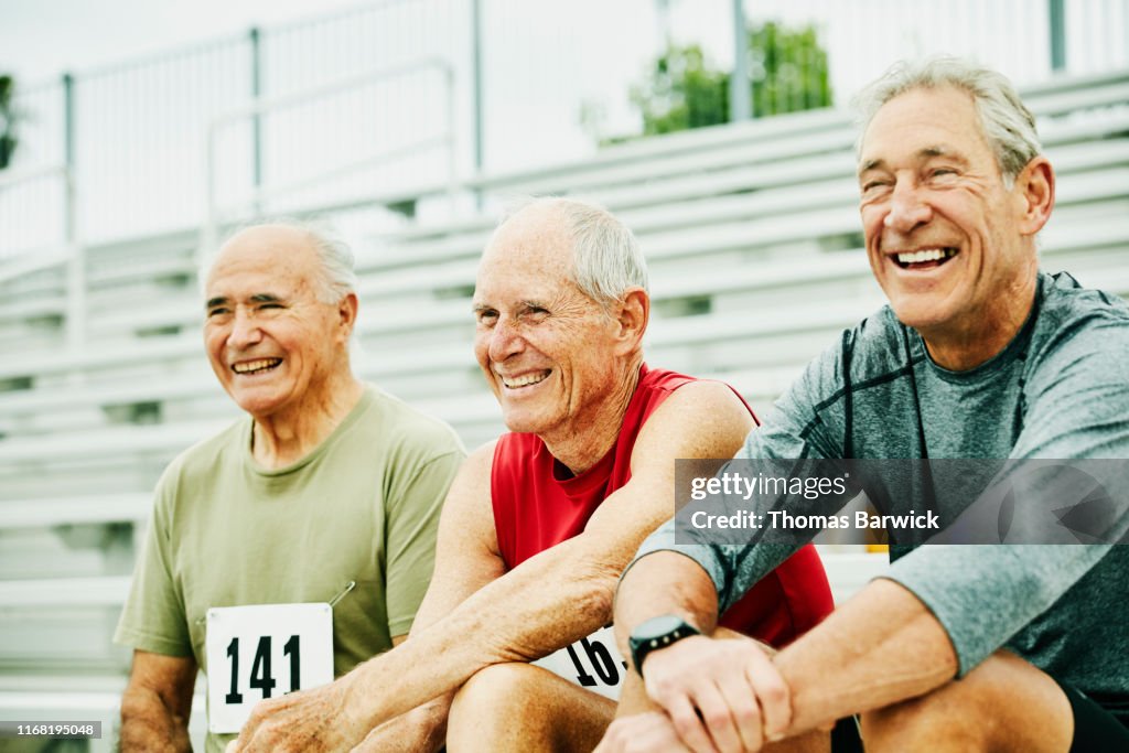 Smiling and laughing senior male track athletes hanging out together on bleachers