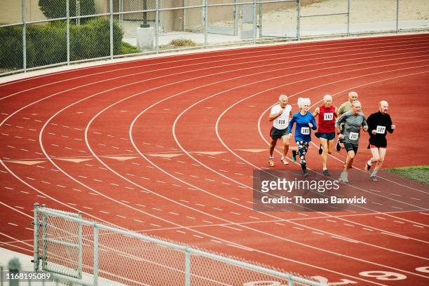 group of senior track athletes running distance race on track - forward athlete stock pictures, royalty-free photos & images