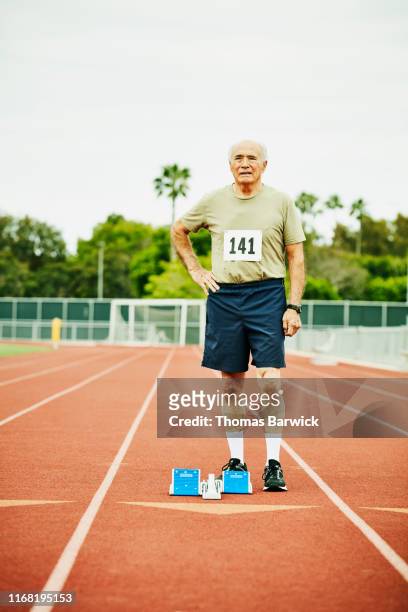 Portrait of senior male track athlete standing next to starting blocks on track