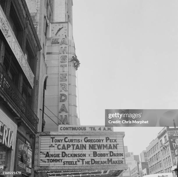 Man cleaning the neon sign at the New Amsterdam Theatre on 42nd Street in New York City, 1964. The marquee is advertising the film, 'Captain Newman...
