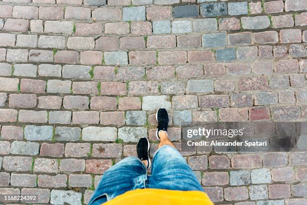 high angle personal perspective view of man in shorts and sneakers walking on a cobbled street - verwonderingsdrang stockfoto's en -beelden