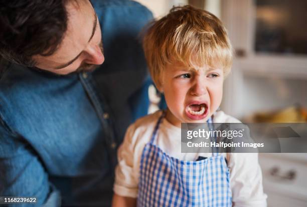a father on paternity leave talking to crying small son indoors. - malumore foto e immagini stock