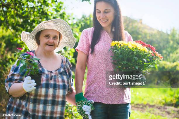 woman with down syndrome and her relative planting flowers together. gardening. - down syndrome care stock pictures, royalty-free photos & images