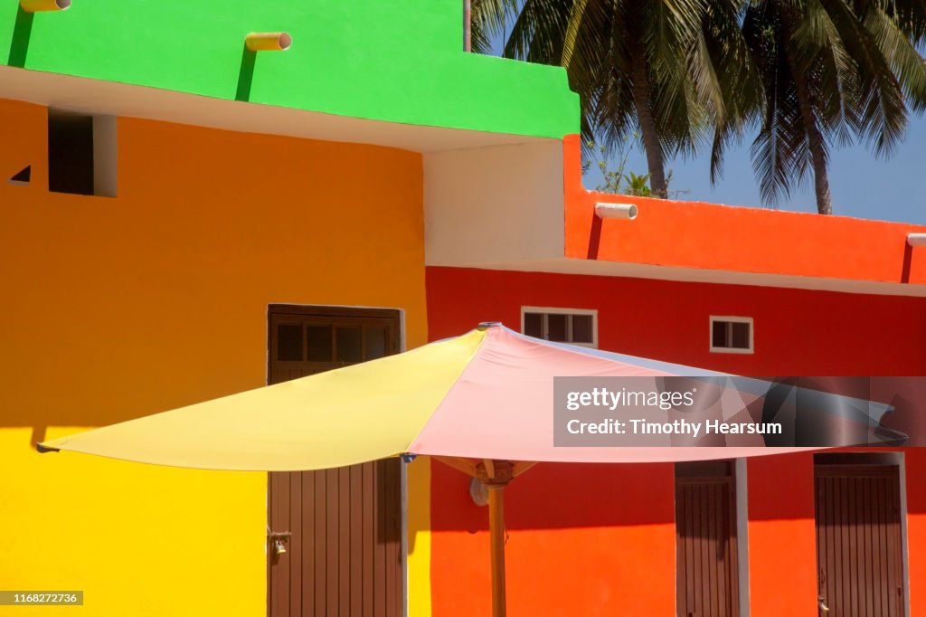 Brightly painted building with colorful umbrella; palm trees in background