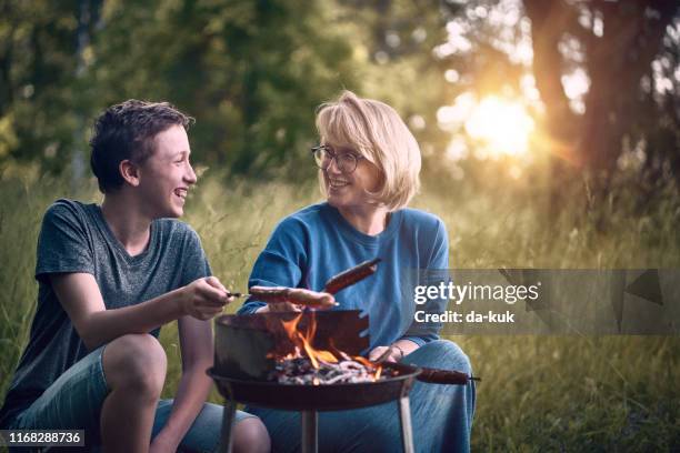 mother and son are cooking sausages on the bbq grill - father sun stock pictures, royalty-free photos & images