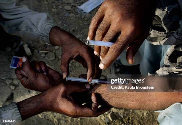 Man injects heroin into a fellow addict's arm October 17, 2001 in the tunnels underneath the roads of dowtown Quetta, Pakistan. Many of Quetta's drug...