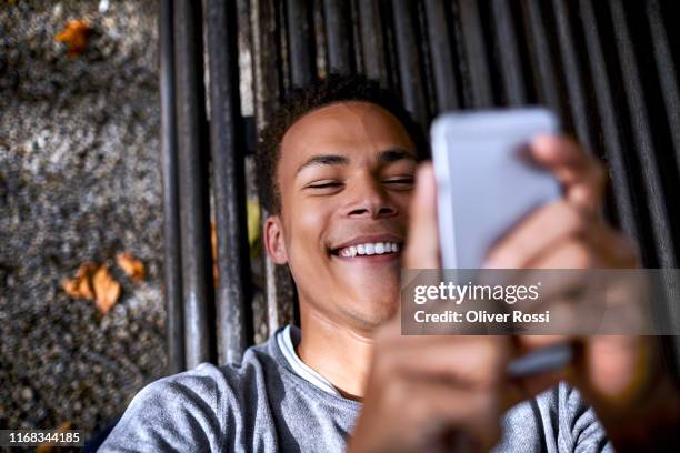 happy teenage boy lying on a bench using cell phone - male looking content stockfoto's en -beelden