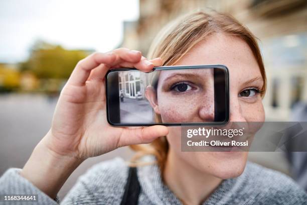 young woman holding smartphone showing her eye - facial recognition technology - fotografias e filmes do acervo