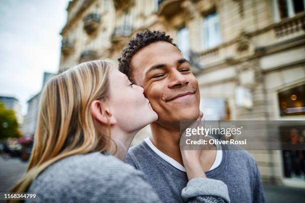 young woman kissing boyfriend in the city - person gemischter abstammung stock-fotos und bilder