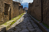 Pompeii, Italy secondary narrow street along remaining houses. Day view of structured formation of cobblestoned path to accommodate traffic inside the town.
