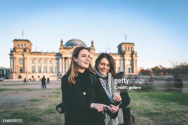 two young woman looking at mobile in front of berlin reichstag - city government stock pictures, royalty-free photos & images