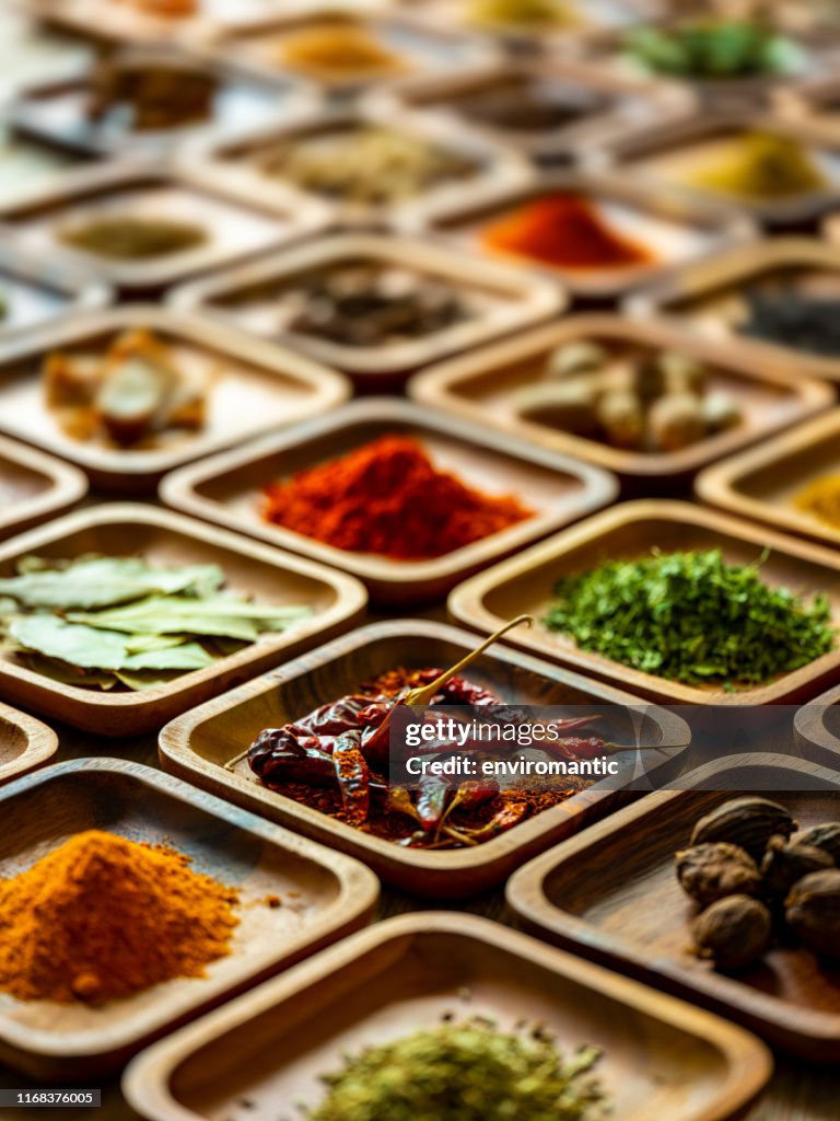 Variety of colorful, organic, dried, vibrant Indian food spices in wooden trays on an old wood background.