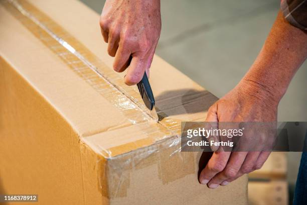 an industrial workplace warehouse safety topic. a female cutting a box using a utility knife. - craft knife stock pictures, royalty-free photos & images
