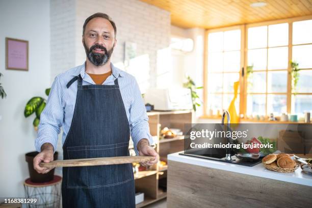 mature bearded man holding wooden tray - apron man stock pictures, royalty-free photos & images